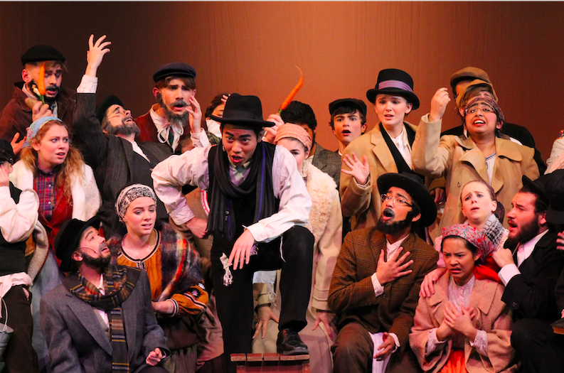 Khoi Do, senior, poses in front of the ensemble during a musical number in Fiddler on the Roof.