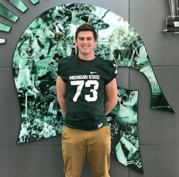 Henrichs poses next to the Michigan State logo while on a campus visit. 