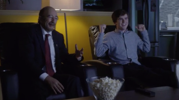 Aaron Glassman, played by Richard Schniff, sits with Murphy Murphy, played by Freddie Highmore, as they watch something on television. 