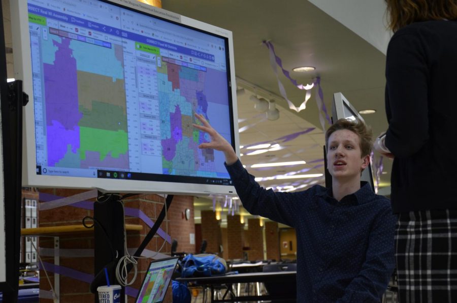 Jack Wypiszynski, senior, kneels down near a map to point out his results on Gerrymandering in Wisconsins State Assembly Compared to a Redrawn Map. 