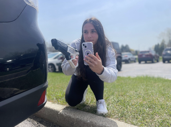 Emmy Sehnert, senior, hides behind her car with her water gun in her right hand and her phone
in her left hand to capture video evidence of her assassinating her target.