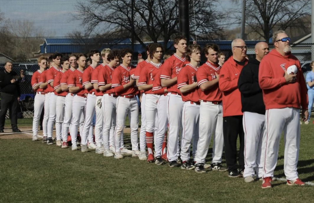 The baseball team starts their game off against Port Washington with the national anthem.