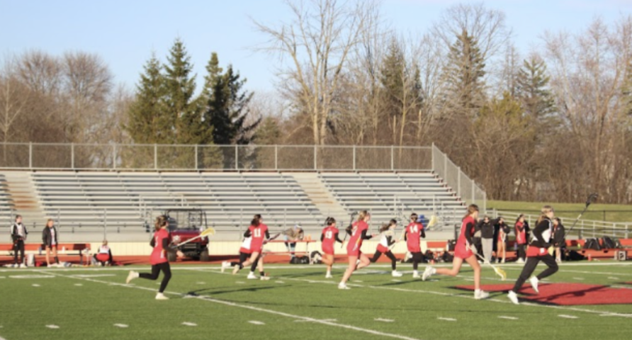 The girls' lacrosse team hustles down the field, trying to score a goal.