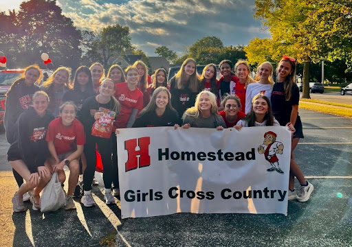 (Left to right) Kelsey Hart, Ella Gotz, Adline Navarre, and Ashlyn Aiello, with their teammates, hold up a sign for Girls Cross Country in the 2025 homecoming parade.

