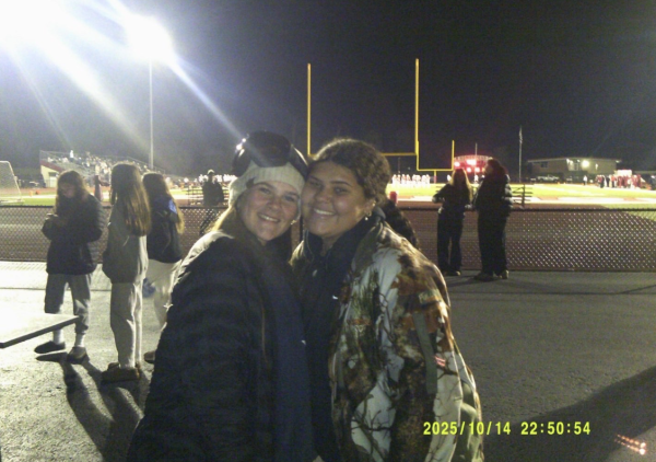 Madi Williams, senior, and Grace Forbes, freshman, pose in front of the Homestead football field.